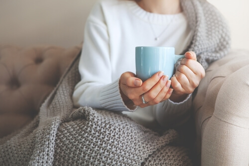 毛布にくるまって暖かい飲み物を飲む女性