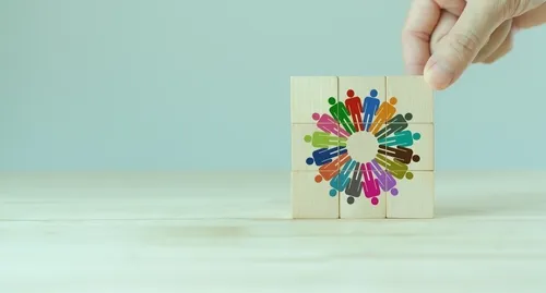 人間が寄り添って輪を作るイラストが描かれた積み木をつかむ手元