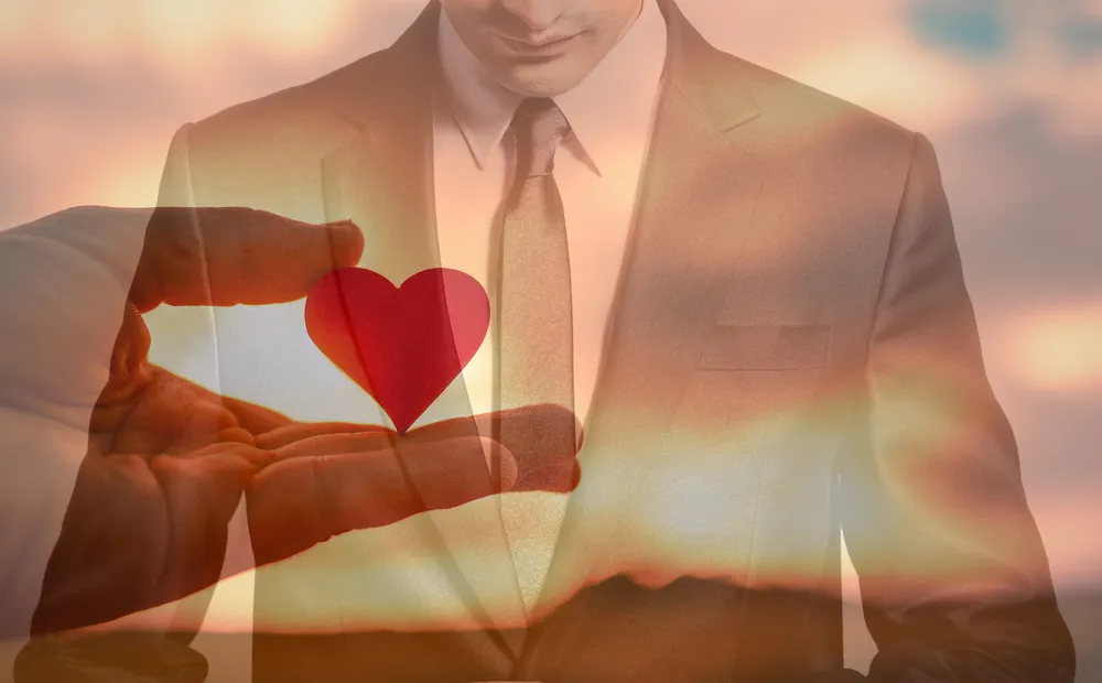 夕日を背景にスーツの人のハートを支える手元のイメージ