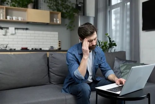 頭を抑えながらソファでPC作業をする人