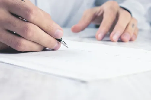 白い服を着た人が紙にペンで書く手元