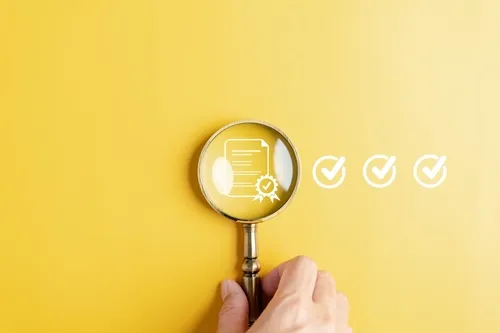 黄色い背景に認定マークを覗く虫眼鏡を持つ手元