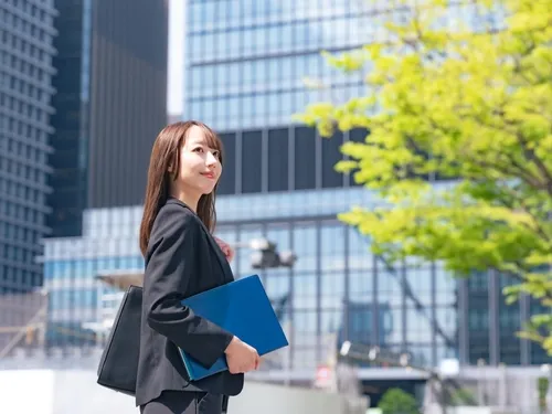 晴れた日にファイルを持って微笑むスーツの女性